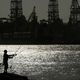 A person fishes in Port Aransas, Texas in front of an offshore oil drilling platform.